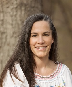 Portrait einer Frau vor einem Naturhintergrund. Sie schaut direkt in die Kamera und lächelt.